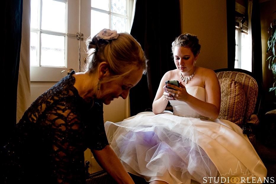 The bride checks her phone as her mom puts her shoes on before her wedding at the House of Blues in New Orleans
