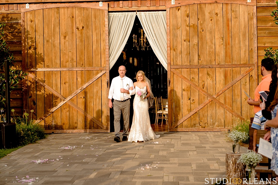 The bride and her father walk out of the barn doors for her wedding ceremony at the Berry Barn